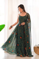 Woman wearing a green and red patterned dress with a sheer dupatta in a bright room.