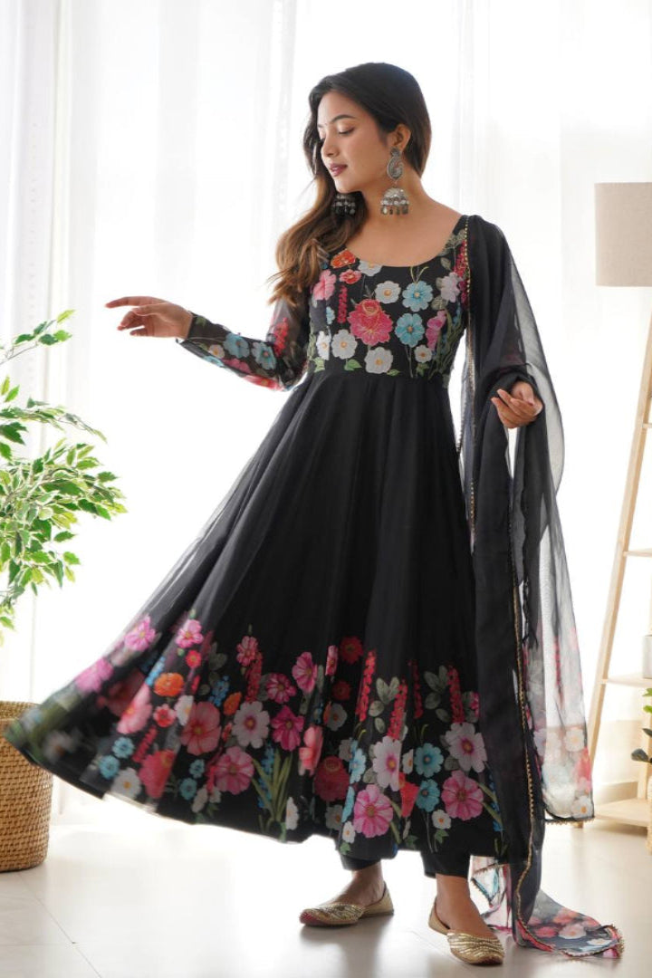 Woman wearing a black floral dress in a bright room with plants and a lamp.