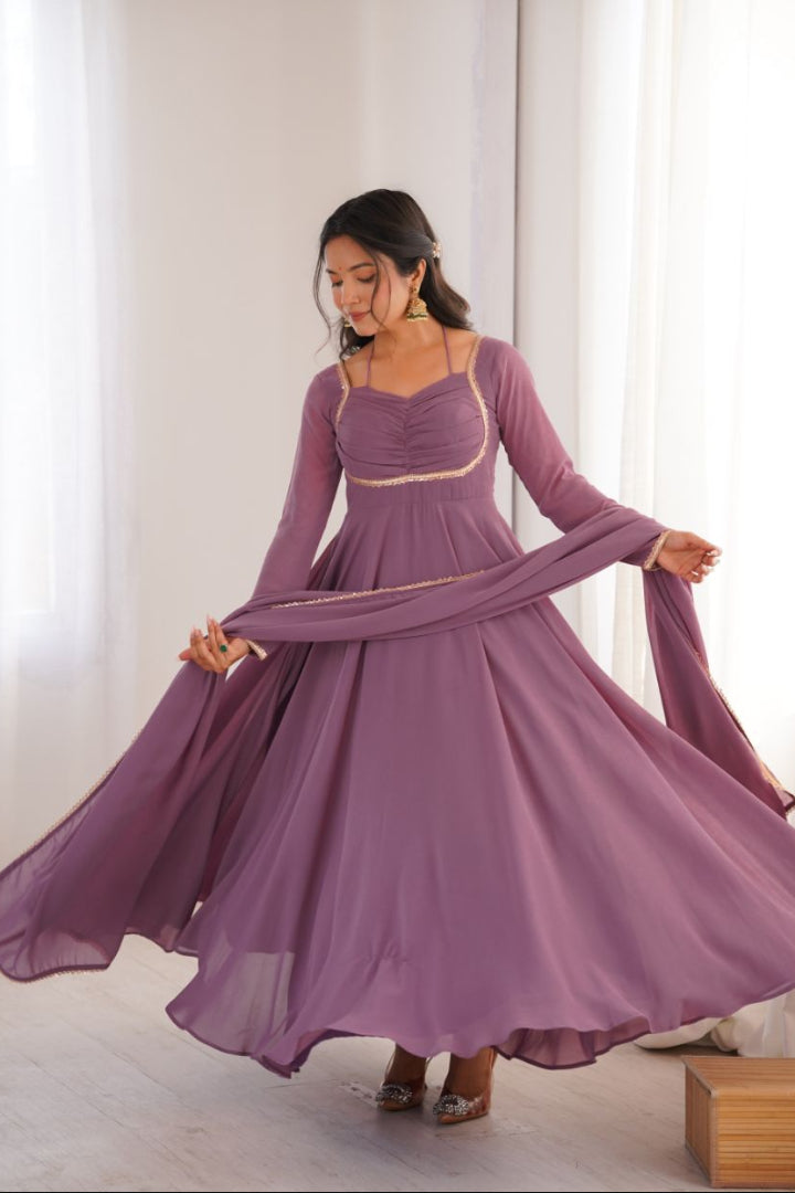 Woman wearing a long purple dress with sheer sleeves in a bright room.