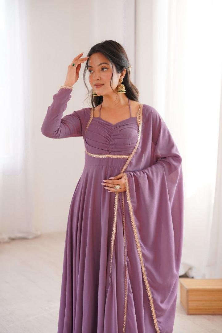 Woman wearing a long purple dress with gold accents in a bright room.
