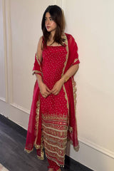 Woman wearing a red traditional outfit with gold details against a white wall.