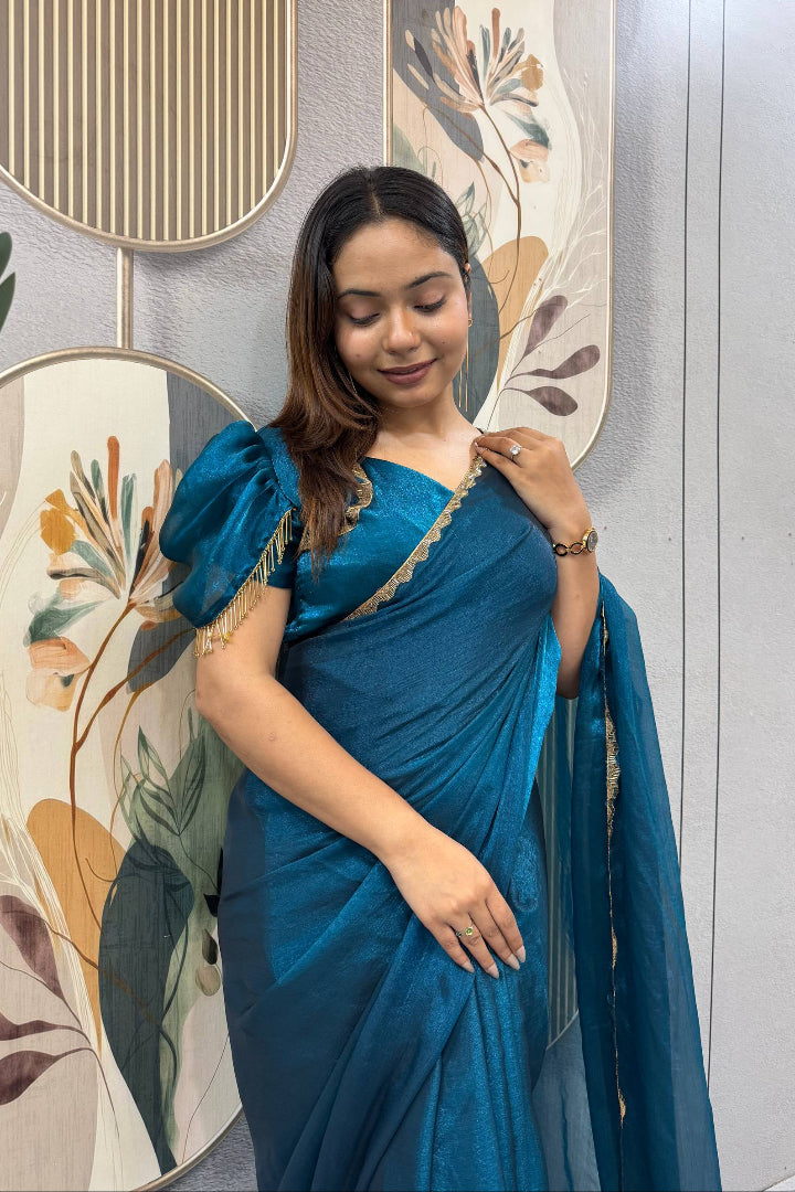 Woman in a blue saree posing in front of decorative wall art