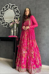Woman in a pink floral dress standing in a room with a decorative mirror and table.
