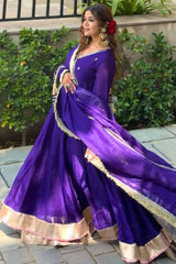 Woman in a purple traditional outfit with gold details standing outdoors.