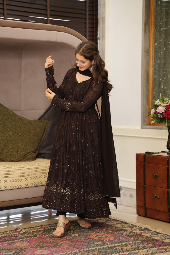 Woman in a dark traditional outfit standing in a room with a sofa and decorative items.