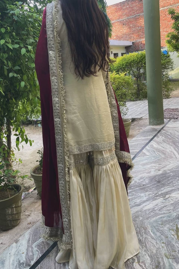 Person wearing a cream traditional outfit with maroon dupatta in an outdoor setting
