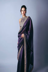 Woman wearing a purple saree with intricate designs on a plain background