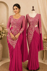 A woman and a mannequin display matching magenta sarees with heavily embroidered light pink and gold sleeves and bodices, set against a warm beige interior backdrop with floral decor.
