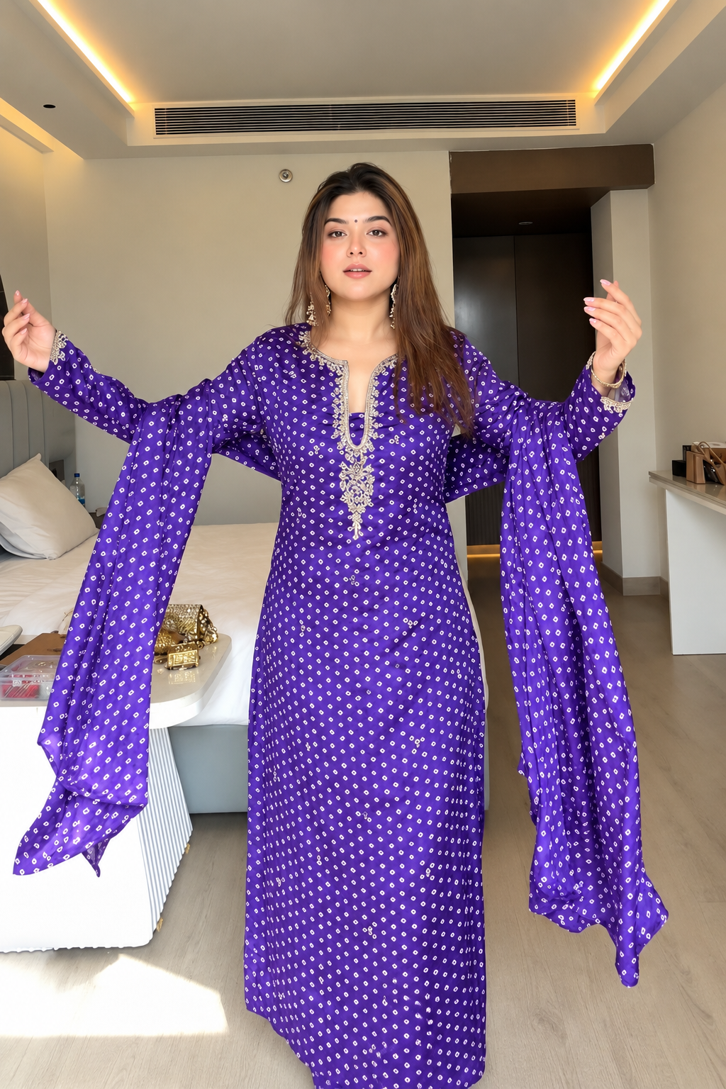 A woman modeling a purple long kurta with white polka dots and silver embellishments, featuring dramatic bell sleeves, in a modern bedroom setting.