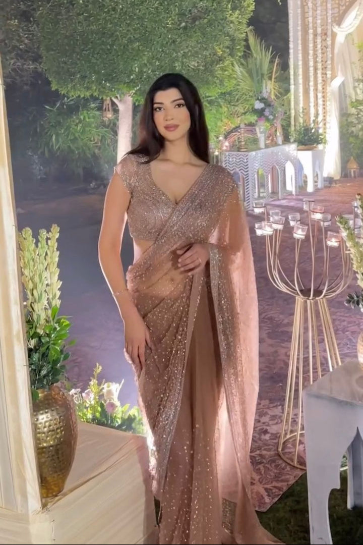 Woman in a sparkling saree standing in an elegant outdoor setting with decorative elements.