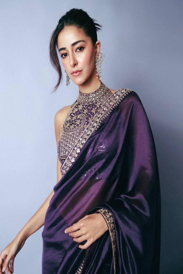 Woman wearing a purple saree with intricate designs against a gray background