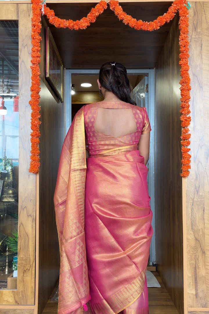 Woman in a pink saree standing in a doorway with decorative marigold garlands.
