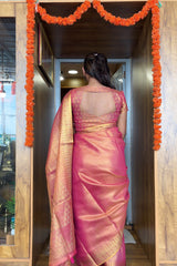 Woman in a pink saree standing in a doorway with decorative marigold garlands.
