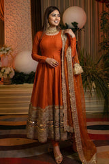 Woman in an orange traditional outfit with intricate designs, standing in a decorated indoor setting.