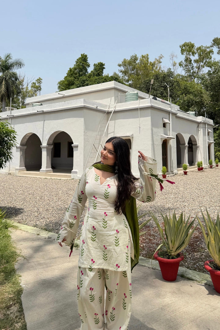 Woman in a white traditional outfit standing in front of a building with greenery around.