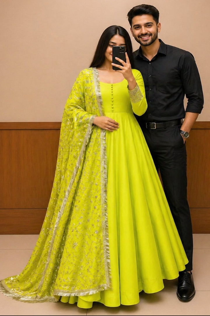 Woman in a bright yellow traditional outfit with a man in a black shirt and pants against a beige wall.