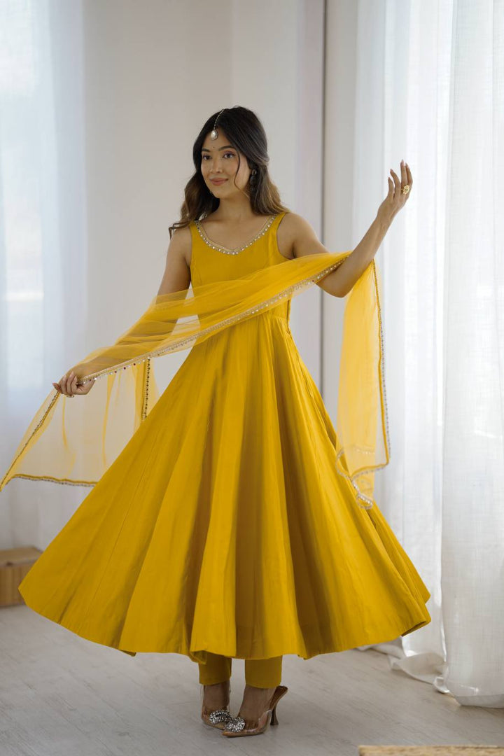 Woman in a yellow dress with a sheer dupatta standing in a bright room.