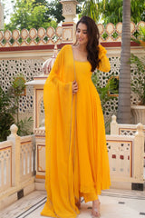 Woman in a yellow dress standing in an outdoor setting with decorative architecture and greenery.