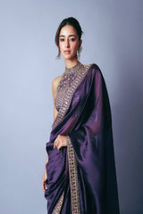 Woman wearing a purple saree with intricate gold detailing on a gray background