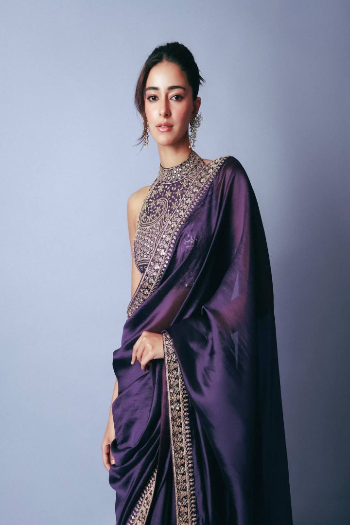 Woman wearing a purple saree with intricate gold detailing on a gray background