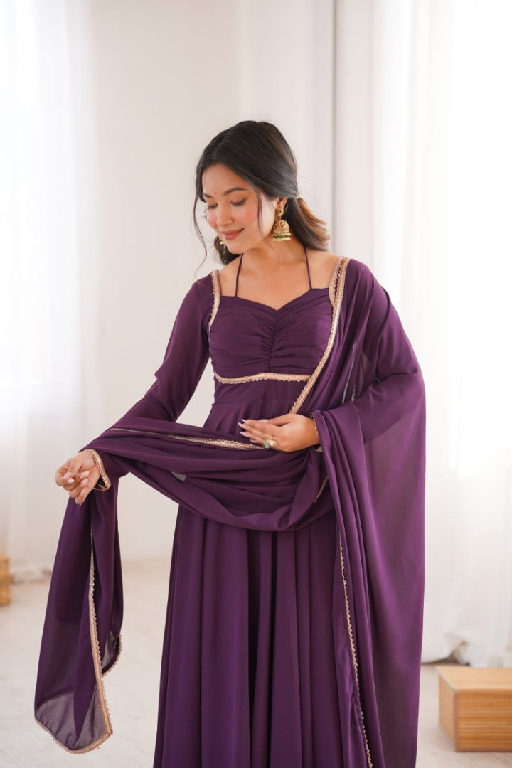Woman wearing a purple dress with gold accents in a bright room.