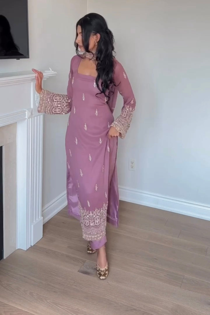 Woman in a purple dress standing in a room with a fireplace.