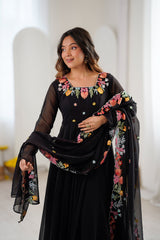 A woman modeling a black traditional outfit with colorful floral embroidery 