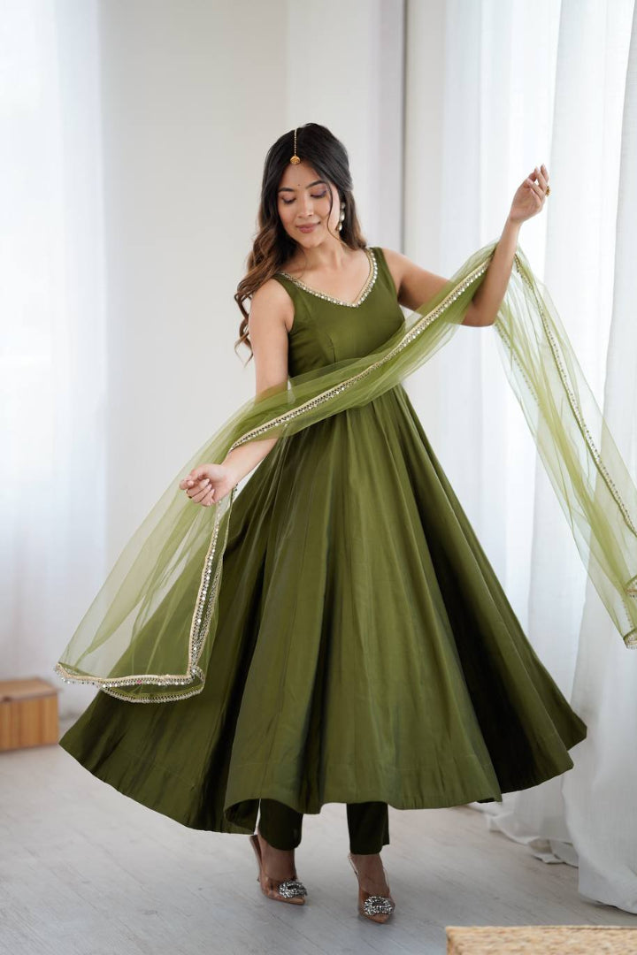 Woman wearing a green traditional outfit with a sheer dupatta in a bright room.