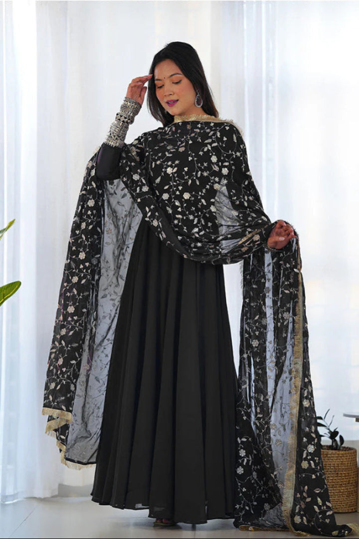 Woman wearing a black traditional outfit with a floral dupatta in a bright room.