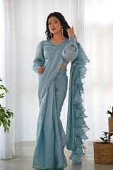 Woman wearing a light blue saree with ruffled edges in a bright room.