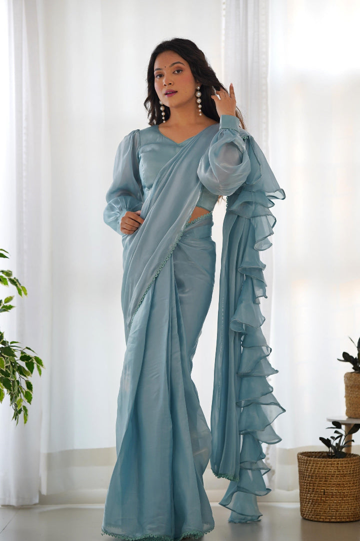Woman wearing a light blue saree with ruffled edges in a bright room.