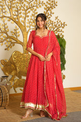 A woman models a red traditional Indian outfit with white polka dots and gold borders, standing in front of a decorative gold tree and cow wall art.