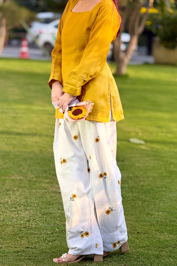 Person wearing a yellow top and white pants with sunflower patterns on grass