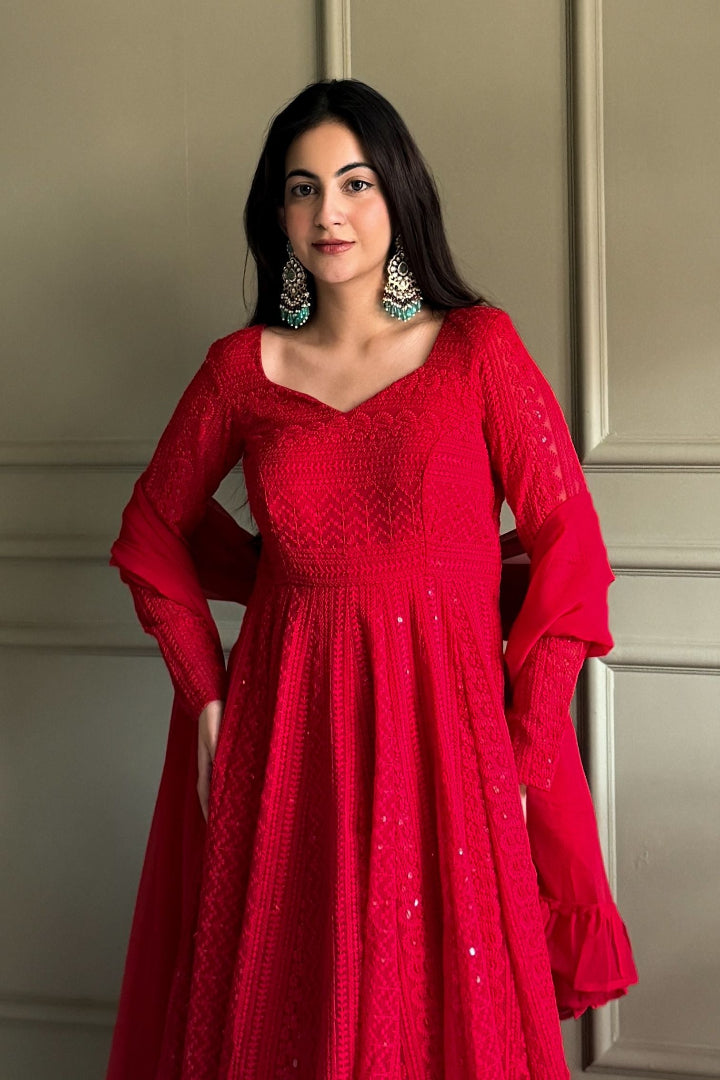 Woman wearing a red dress with intricate patterns against a neutral background