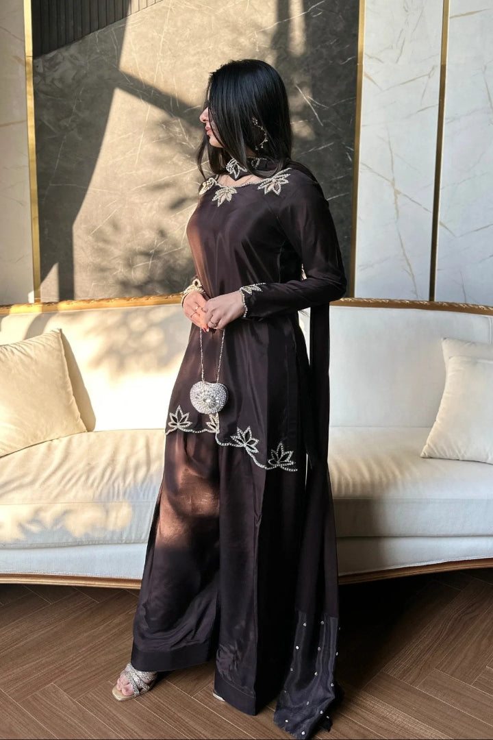 Woman in a long black dress with white embroidery standing in a stylish room.
