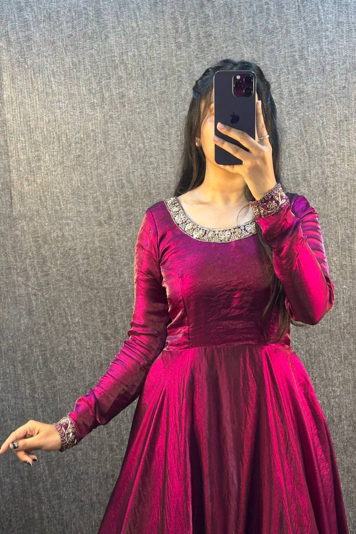 Person wearing a pink dress with long sleeves and a textured gray wall background