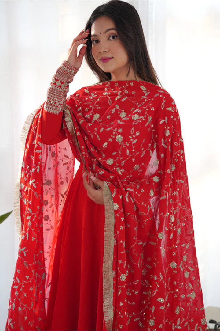 Woman wearing a red traditional outfit with floral patterns indoors.