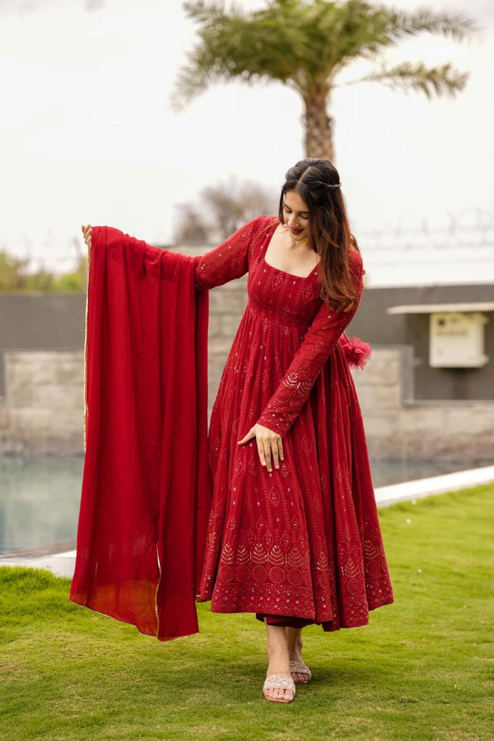 Woman in a red dress holding a matching dupatta on a grassy area with a pool and palm tree in the background.