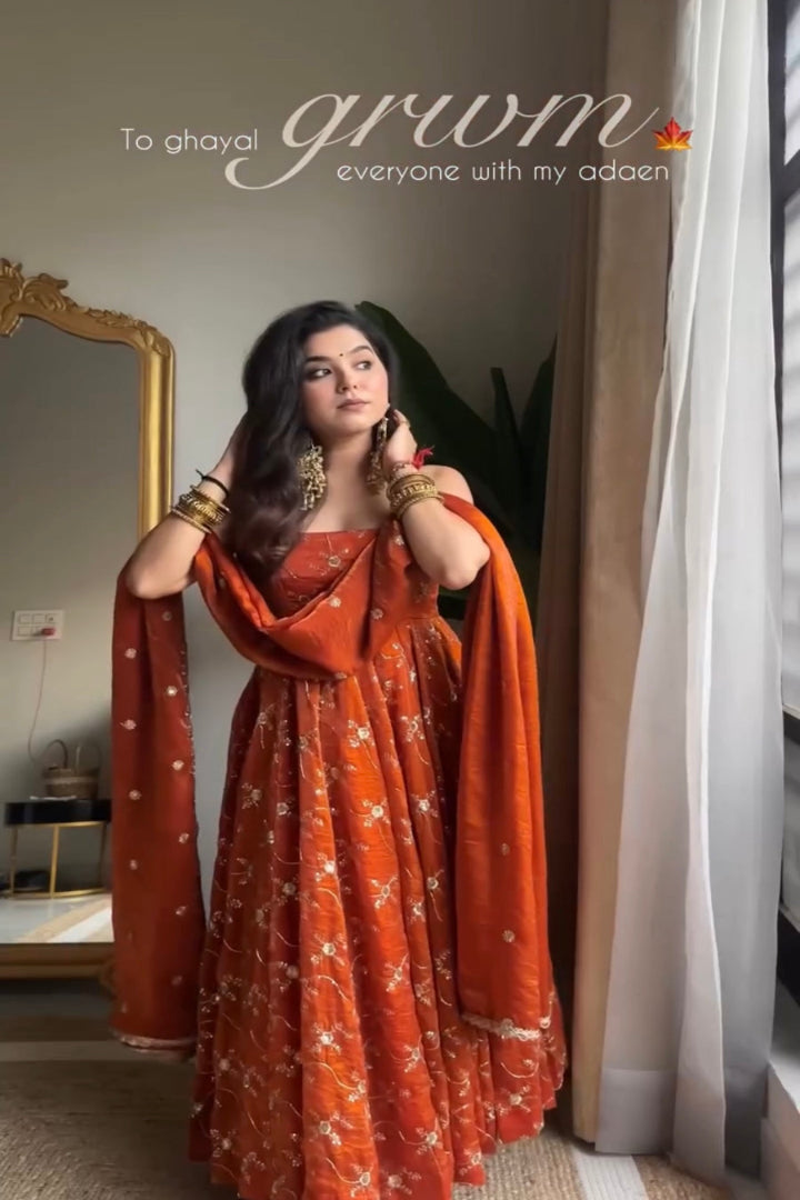 Woman in an orange traditional outfit standing in a room with a mirror and curtains.
