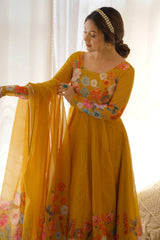Woman wearing a yellow floral dress holding a dupatta in a softly lit room.