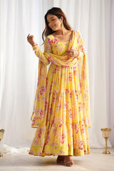 Woman wearing a yellow floral dress with a matching dupatta against a white curtain background
