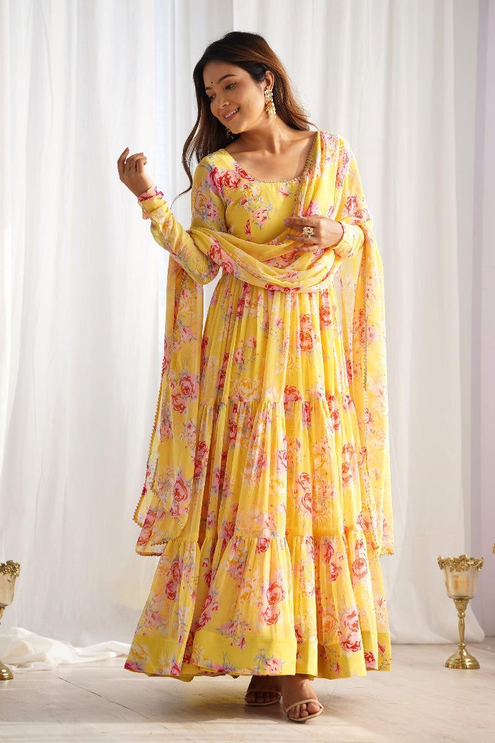 Woman wearing a yellow floral dress with a matching dupatta against a white curtain background
