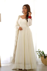 Woman wearing a long white dress with a shawl in a bright room.