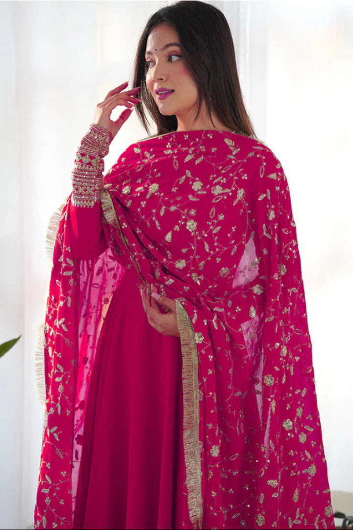 Woman wearing a bright pink traditional outfit with a matching dupatta indoors.