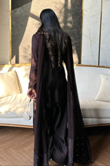 Person wearing a long dark coat standing in a room with a white couch and decorative wall.