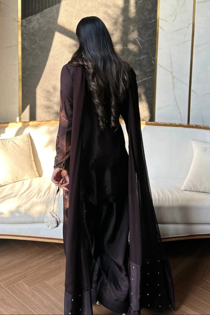 Person wearing a long dark coat standing in a room with a white couch and decorative wall.
