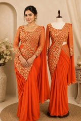An orange saree with intricate gold floral embroidery on the bodice and sleeves, shown both modeled by a woman and displayed on a mannequin in a styled indoor setting.