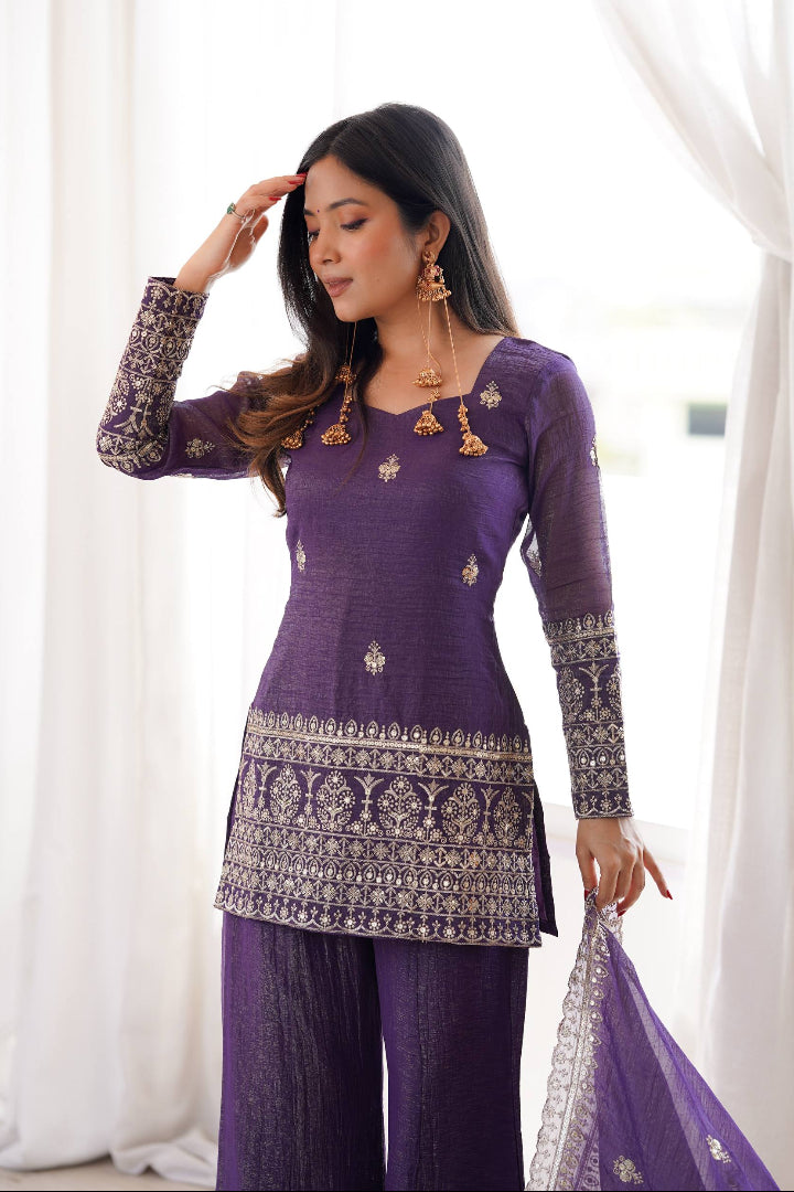 Woman wearing a purple traditional outfit with intricate designs against a white curtain background