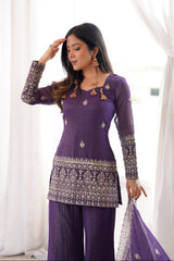 Woman wearing a purple traditional outfit with intricate designs against a white curtain background
