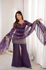 Woman in a purple traditional outfit with a sheer dupatta against a white curtain background